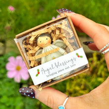 Hand holding a small wooden angel figurine in a box with a green outdoor background