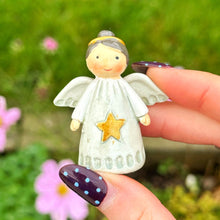 Hand holding a small angel figurine with a star, against a blurred green outdoor background.