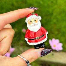 Hand holding a small Santa Claus figurine with a green grass background