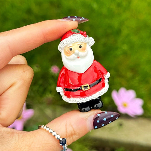 Hand holding a small Santa Claus figurine with a green grass background