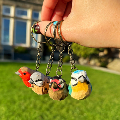 Hand holding a keychain with four bird-shaped charms against a grassy outdoor background