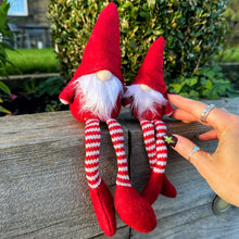 Two red gnome figurines with white beards and striped legs on a wooden surface outdoors.