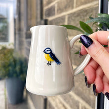 White ceramic pitcher with a bird design held by a hand against a brick wall background