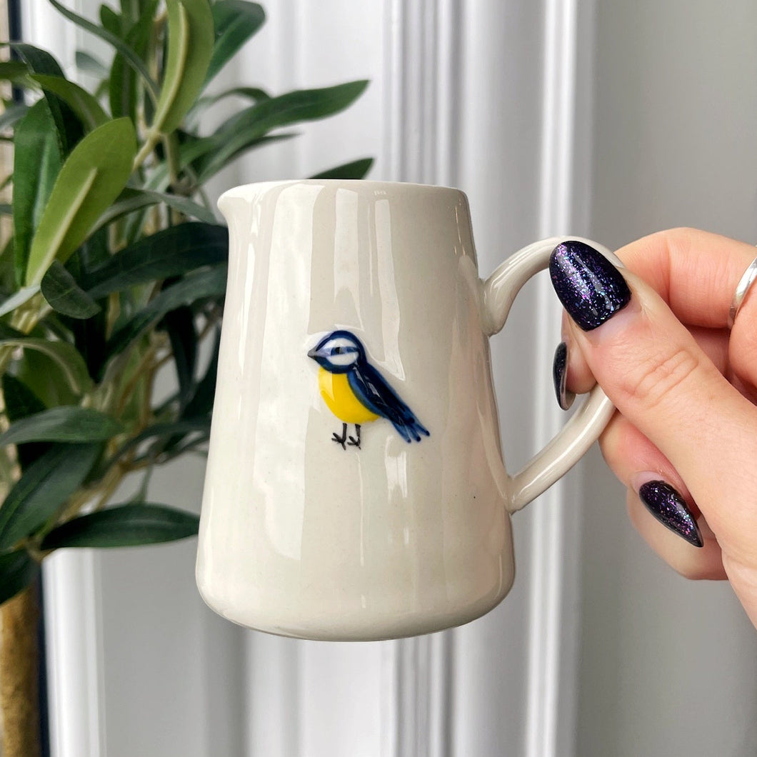 Person holding a white mug with a bird design in front of a window with blinds.