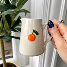 White ceramic mug with orange design held by a hand, plant and window in the background