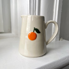White ceramic pitcher with an orange design on a white surface