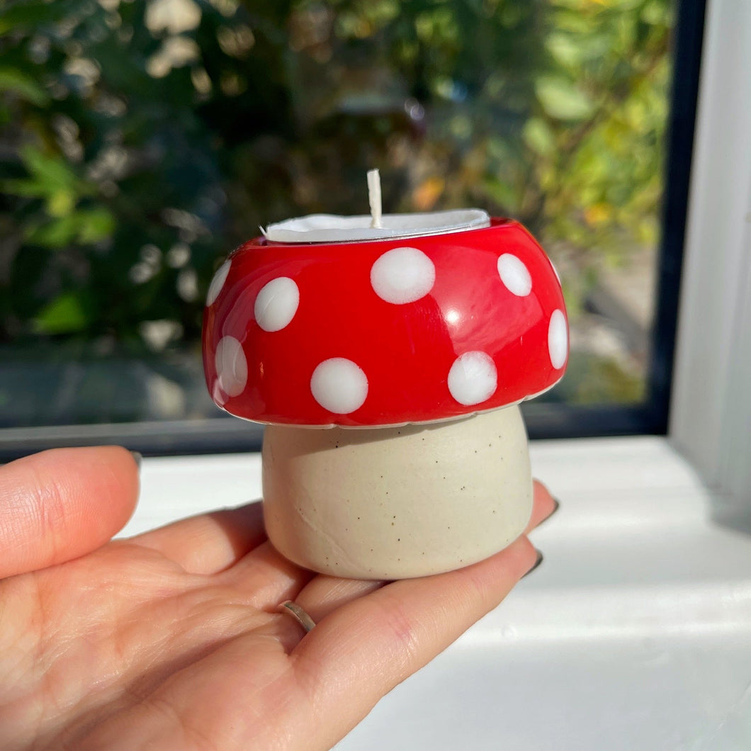 Hand holding a small mushroom-shaped candle with a red cap and white polka dots.