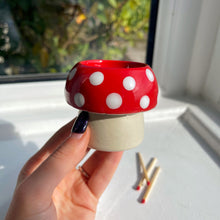 Red and white polka dot mushroom-shaped object held by a hand on a light surface.