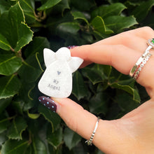 Hand holding a small white angel figurine with 'My Angel' text against a green leafy background