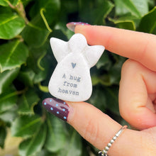 Small angel-shaped object with 'A hug from heaven' text held by a hand against a green leafy background