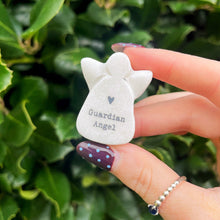 Hand holding a small white 'Guardian Angel' figurine against a green leafy background