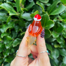Hand holding a small red and white figurine against a green leafy background