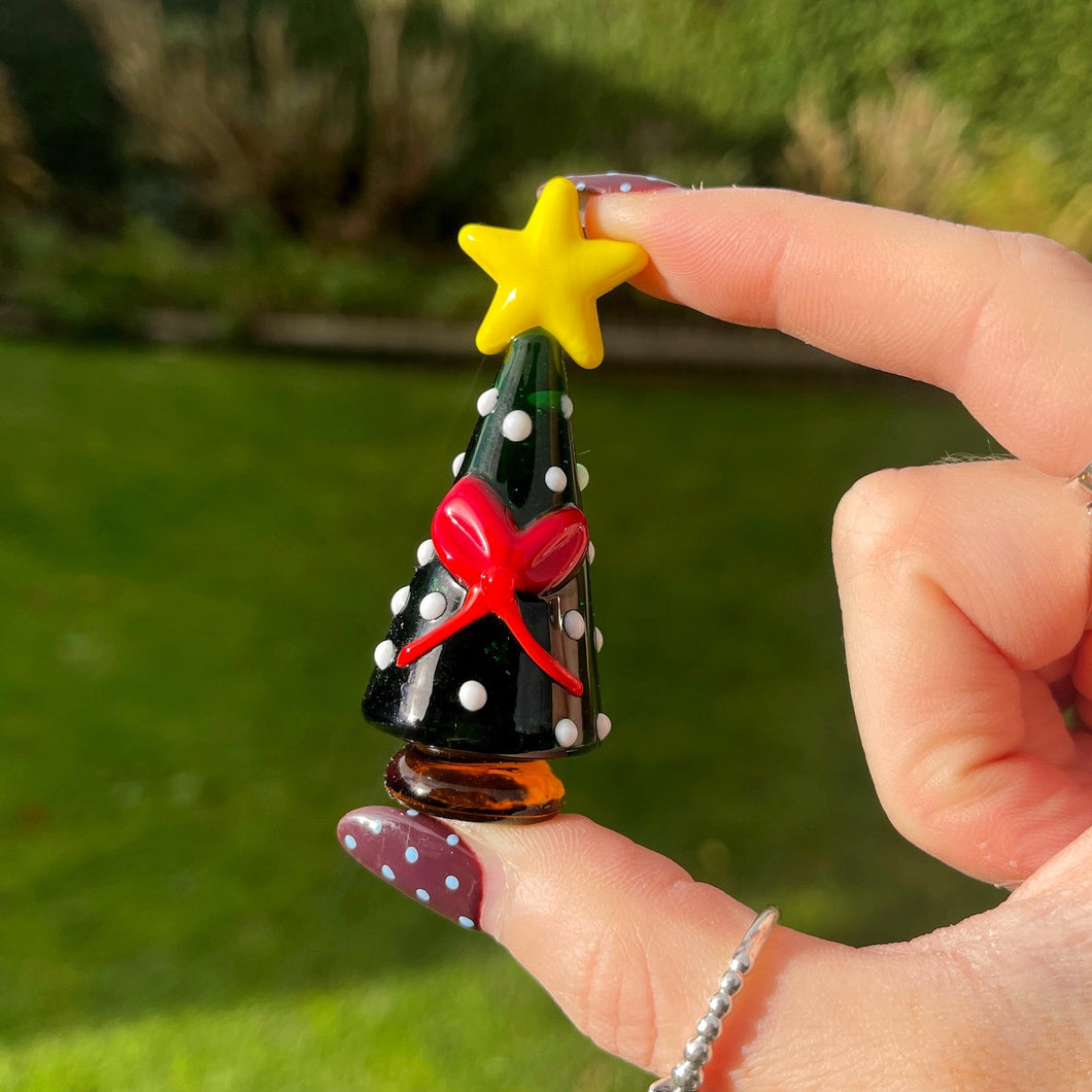 Hand holding a small Christmas tree ornament with a yellow star on a grassy background