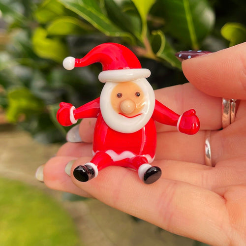 Hand holding a small Santa Claus figurine with a blurred green outdoor background