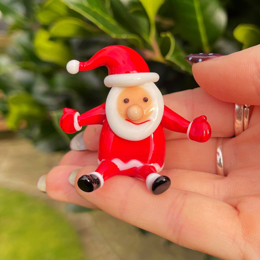 Hand holding a small Santa Claus figurine with a blurred green outdoor background