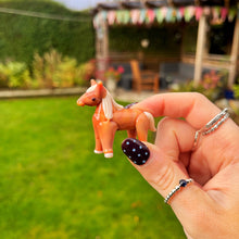 Hand holding a small orange horse figurine with a garden in the background
