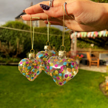 Heart-shaped clear ornaments with colorful dots held by a hand outdoors.