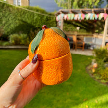 Person holding a peach-shaped orange container outdoors with a garden background