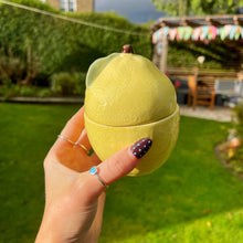 Hand holding a yellow spherical container with a garden in the background