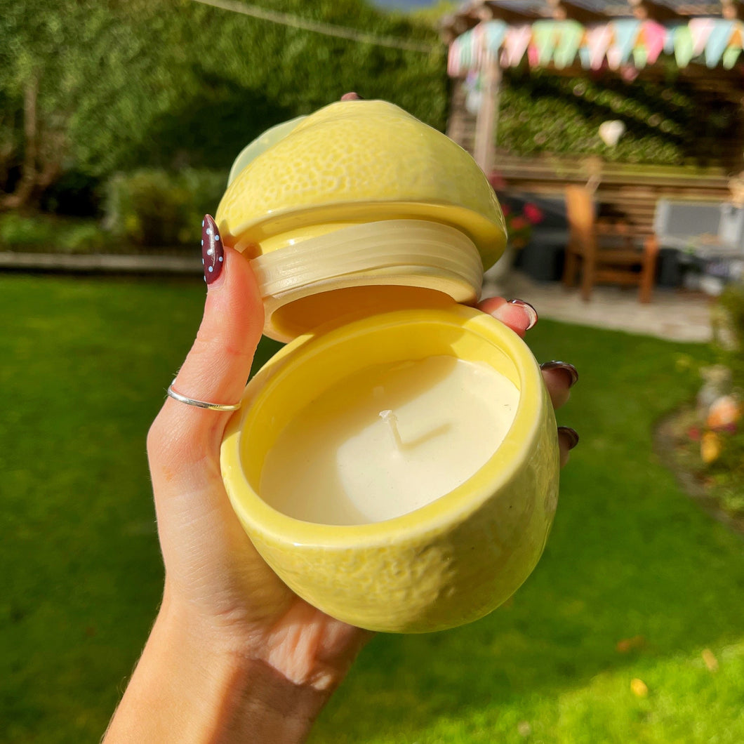 Yellow lemon-shaped candle held by a hand outdoors with greenery in the background