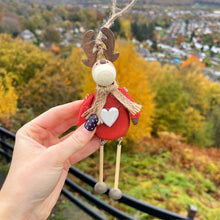 Decorative ornament with reindeer design held against a scenic autumn background.