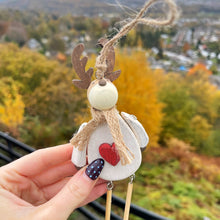 Decorative reindeer ornament held by a hand with autumn trees in the background