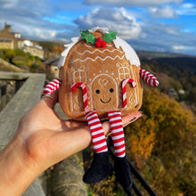 Gingerbread house plush toy with striped legs held against a scenic background