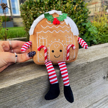Gingerbread house toy with candy cane legs held by a hand outdoors.