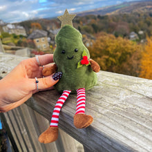 Plush avocado toy with a star on its head and red flower, held by a hand on a wooden railing with a scenic background.