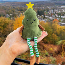 Plush toy resembling a green tree with a star on top, held against an autumn landscape.