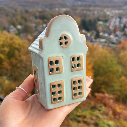 Hand holding a small ceramic house against an autumn landscape