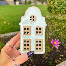 Hand holding a house-shaped cookie with a garden background