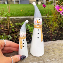 Two small snowman figurines with scarves on a wooden surface outdoors.
