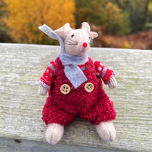 Stuffed animal mouse in a red outfit with buttons, sitting on a wooden surface with autumn foliage in the background.