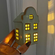 Small house-shaped light held by a hand with a neutral background