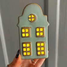 Hand holding a cookie shaped like a house with lit windows against a plain background