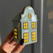 House-shaped light with glowing windows held by a hand against a neutral background