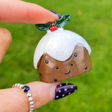 Hand holding a small decorative Christmas pudding figurine against a grassy background