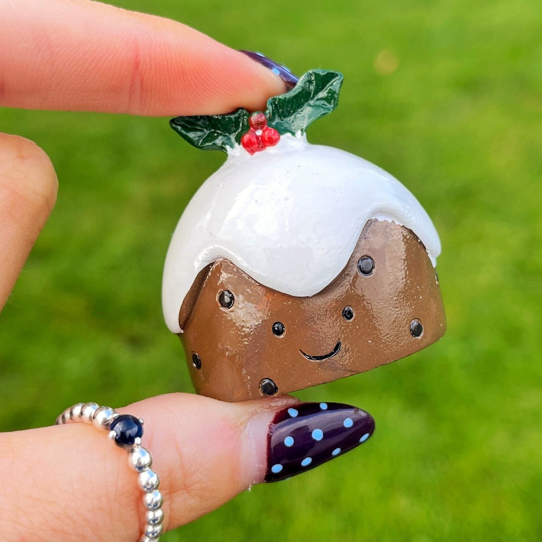 Hand holding a small decorative Christmas pudding figurine against a grassy background