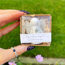 Hand holding a small box with a guardian angel figurine against a green outdoor background