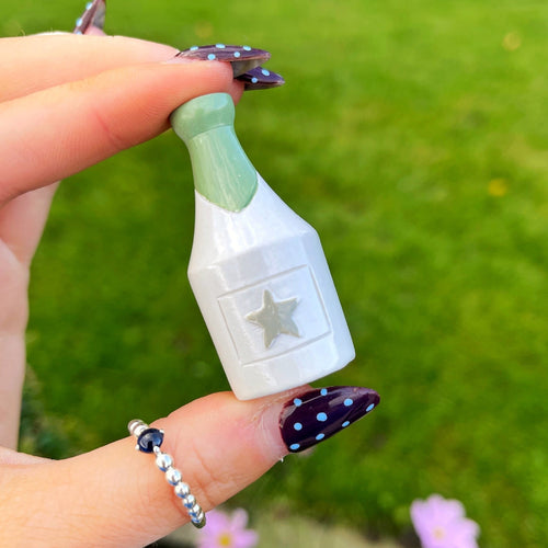 Hand holding a small bottle-shaped object with a star design against a green outdoor background.