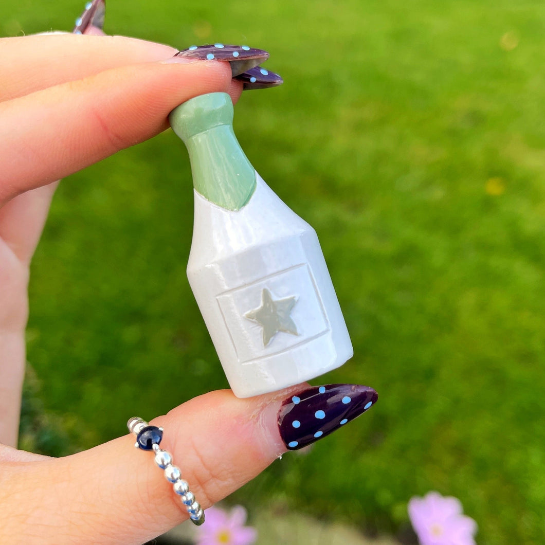 Hand holding a small bottle-shaped object with a star design against a green outdoor background.