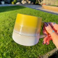 Hand holding a yellow and white mug outdoors on a grassy area
