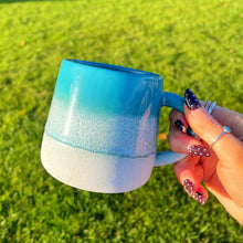 Hand holding a blue and white mug with a grassy background