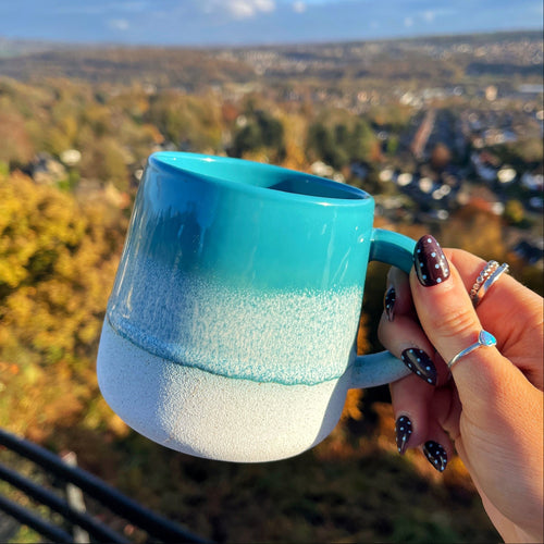 Hand holding a blue and white mug with a scenic view in the background