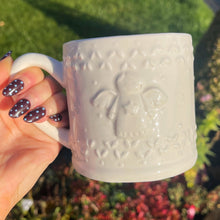 White textured mug held by a hand with decorative nails outdoors.