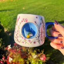 Person holding a decorative mug with floral patterns and a blue handle outdoors.
