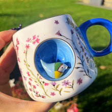 Decorative mug with floral patterns and a blue interior, held outdoors.