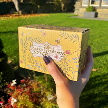 Hand holding a yellow box with floral design and 'Secret Garden' text, outdoors.