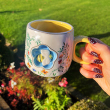 Person holding a decorative mug with a bee design in a garden setting